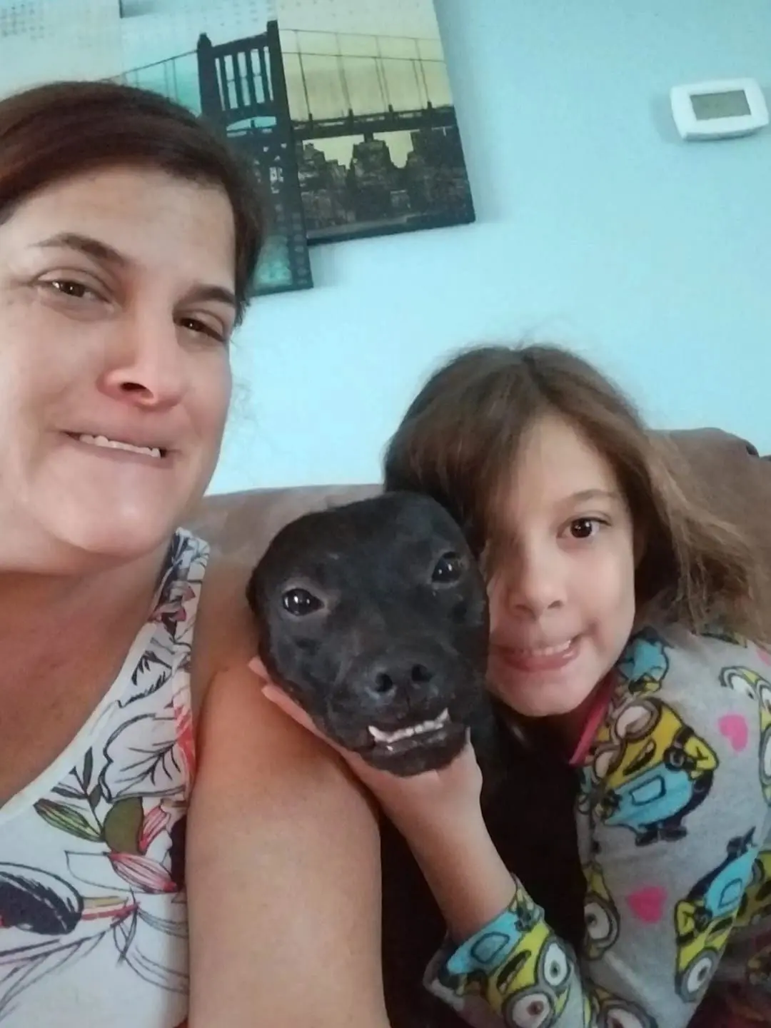 Woman, child, and dog smiling on couch.