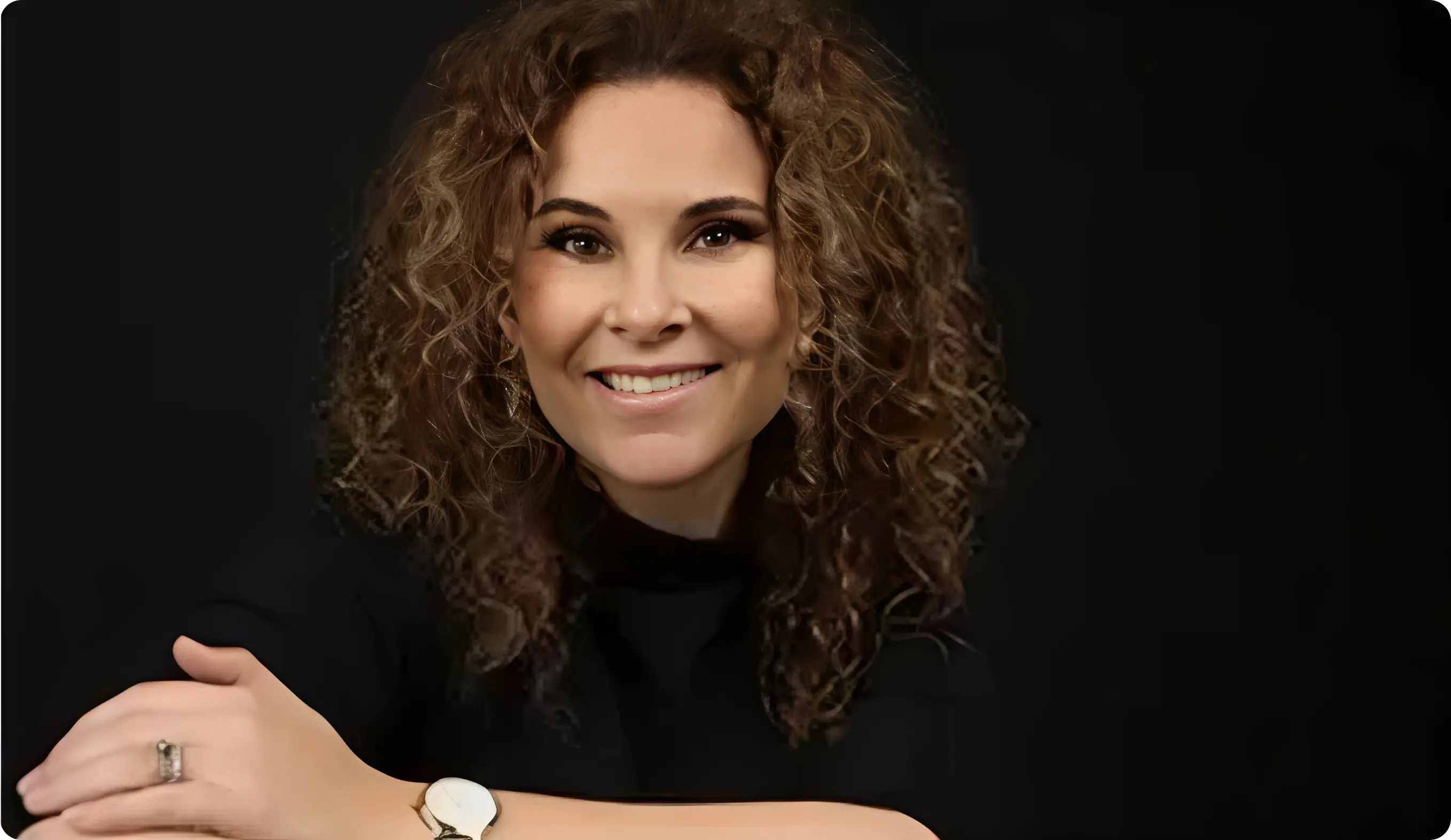 Smiling woman with curly hair, black background.